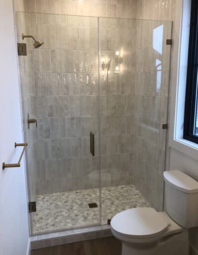 Brushed bronze frameless glass shower door with clear inline panel and square hardware
